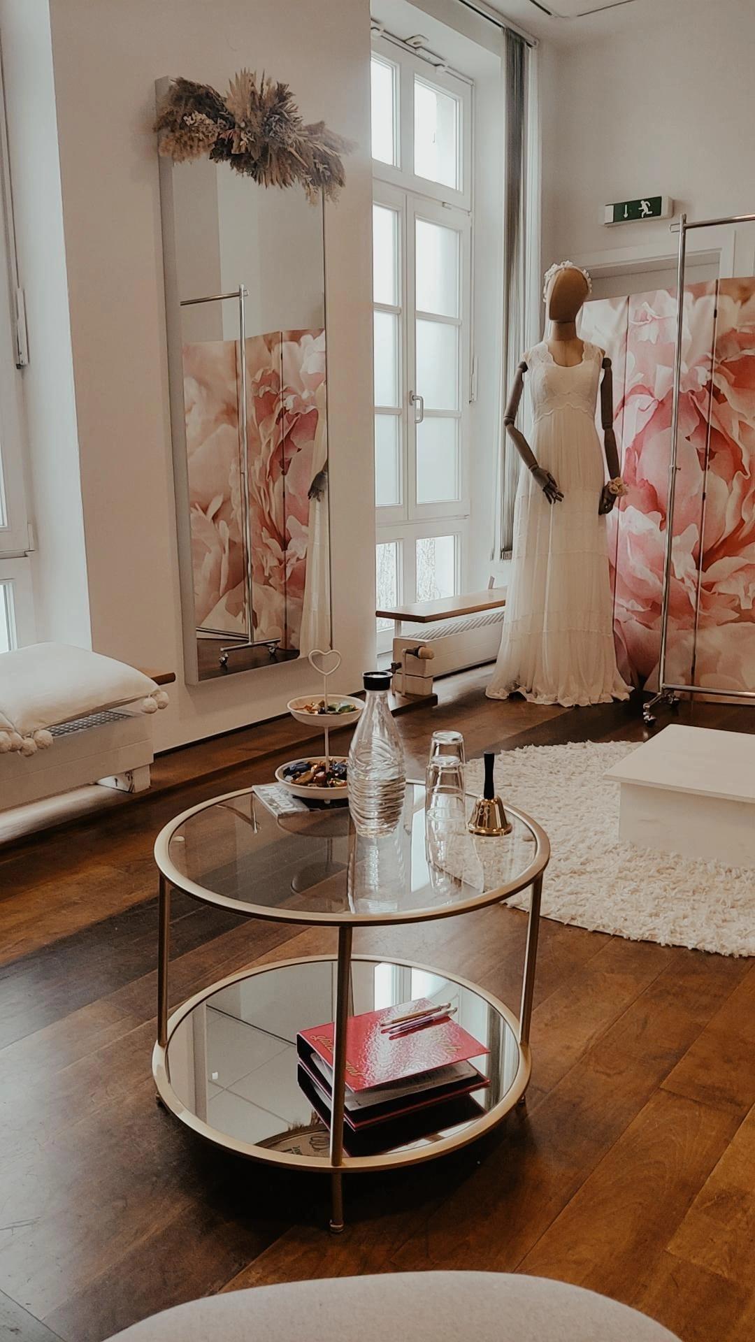 Ein elegantes Brautmodenstudio mit einem auf einem Ständer präsentierten Brautkleid und einem stilvollen Tisch. Der Raum strahlt eine entspannte Atmosphäre aus.