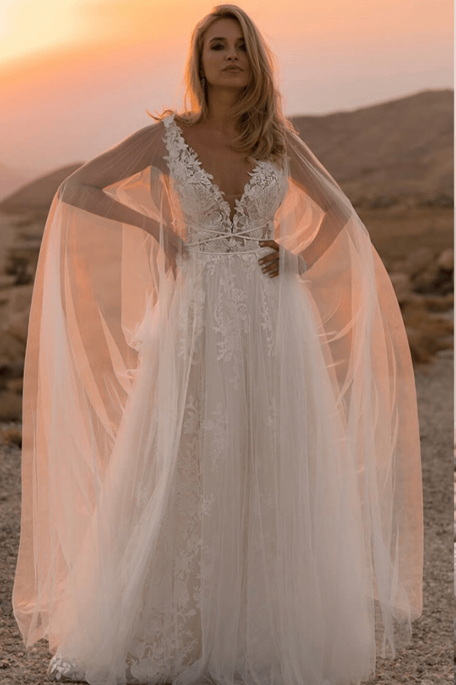 Elegantes Brautkleid im Sonnenuntergang Eine Braut trägt ein elegantes, weißes Hochzeitskleid mit Spitzenakzenten vor einer dramatischen landschaftlichen Kulisse bei Sonnenuntergang.