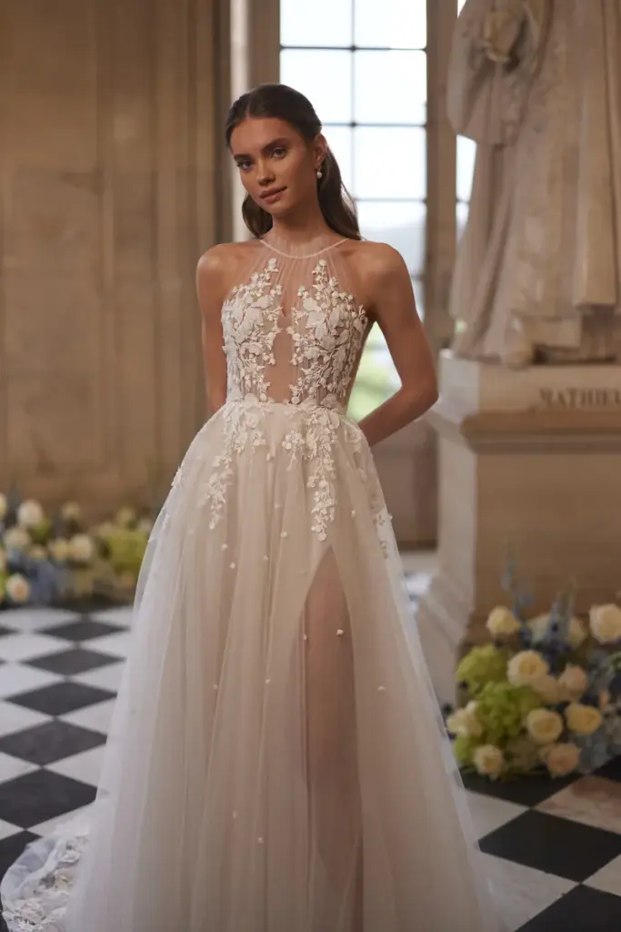 Nahaufnahme eines Brautkleides: über einem Spitzenunterkleid liegt ein transparenter Tüllrock mit eingestickten Perlen und hohem Beinschlitz.