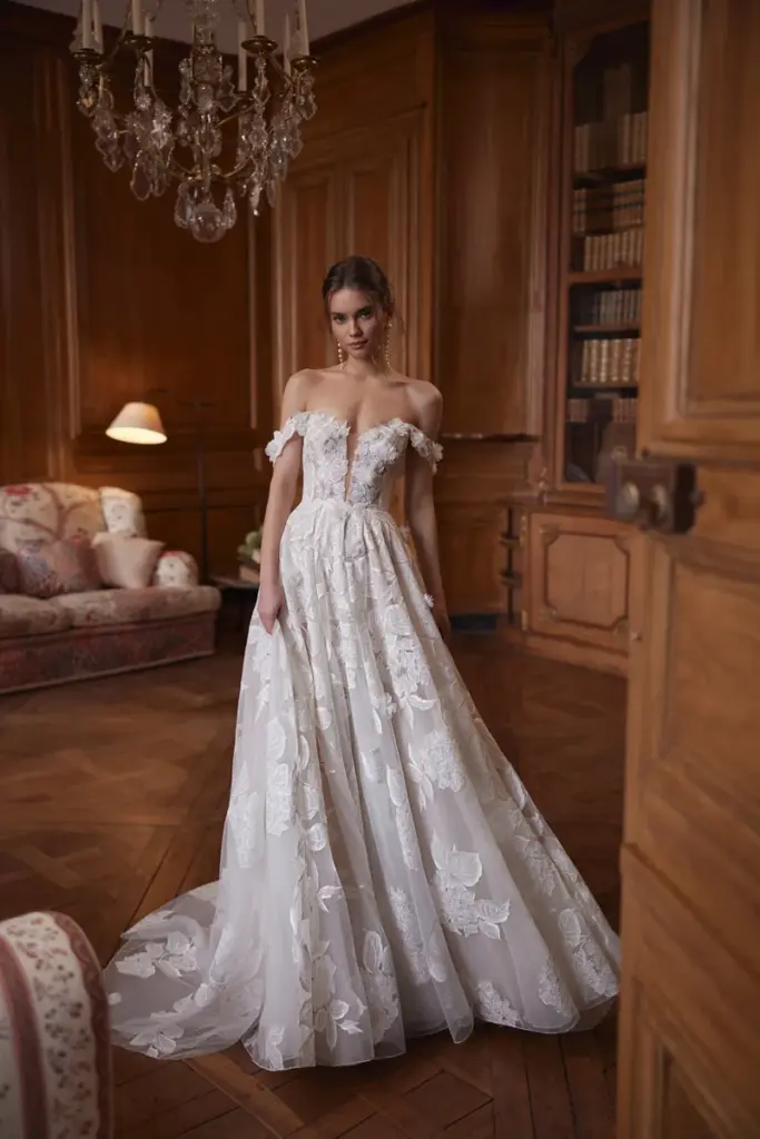 Ein Brautkleid mit großen floralen Spitzenapplikationen und schulterfreien Flatterärmeln; der weite Rock läuft in eine lange Schleppe aus.