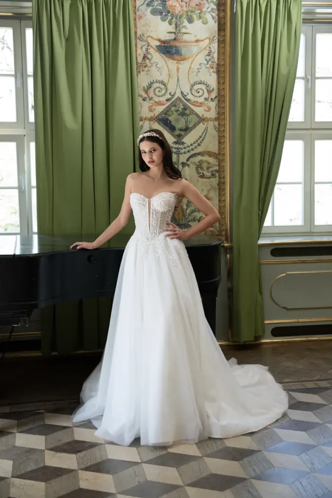Eine Braut am Flügel in einem Brautkleid mit Korsagen-Oberteil aus Blütenspitze und weit ausgestelltem Tüllrock mit langer Schleppe.