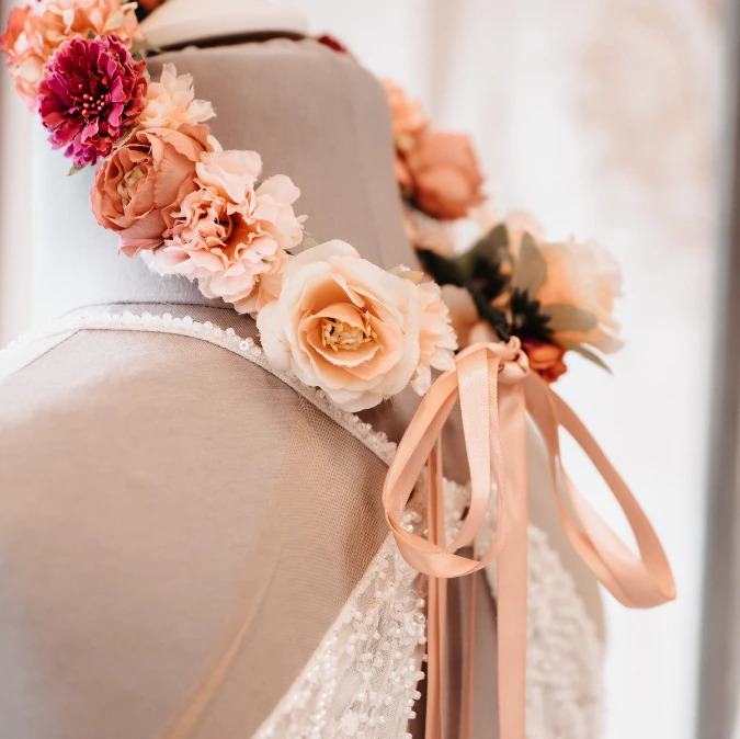 Eine Stoffpuppe im Brautmodenstudio trägt eine zarte, blütenverzierte Halskette mit rosafarbenen Blumen und Bändchen, die den eleganten Stil unterstreichen.