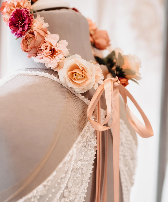 Ein Brautkleid auf einer Schneiderpuppe, geschmückt mit zarten Rosen und einem satinartigen Band. Die Applikationen unterstreichen die Eleganz der Hochzeitsmode.