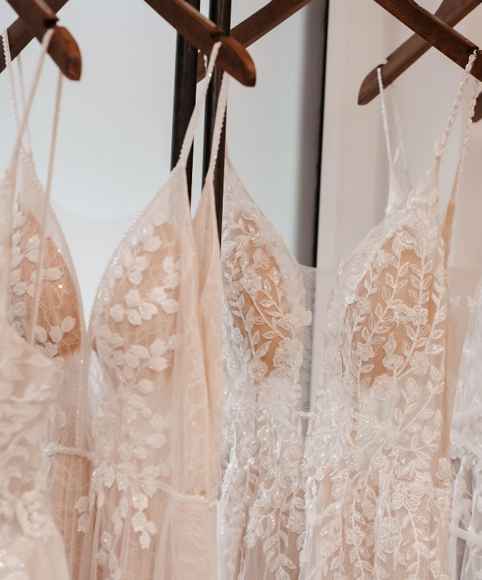 Zwei elegante Brautkleider hängen an einem Holzkleiderbügel. Die Kleider sind mit zarten, floralen Stickereien verziert und strahlen eine romantische Atmosphäre aus.