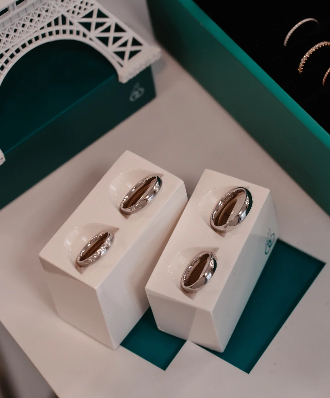 Zwei elegante Eheringe liegen neben einer Miniatur des Eiffelturms auf einem Tisch. Die Ringe präsentieren ein modernes Design und glänzende Oberflächen.
