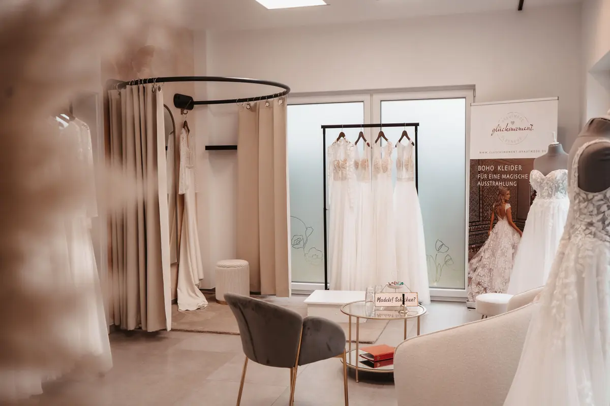 Die Anprobe-Ecke im Studio von Glücksmoment Brautmode in Oldenburg mit Vorhang, Sessel und Beistelltisch, daneben Brautkleider auf Büsten.