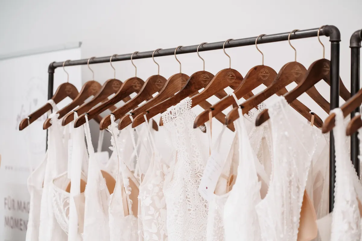 Eine Stange mit Brautkleidern an Holzbügeln im Studio von Glücksmoment Brautmode in Oldenburg, Spitze und fließende Stoffe dicht an dicht.