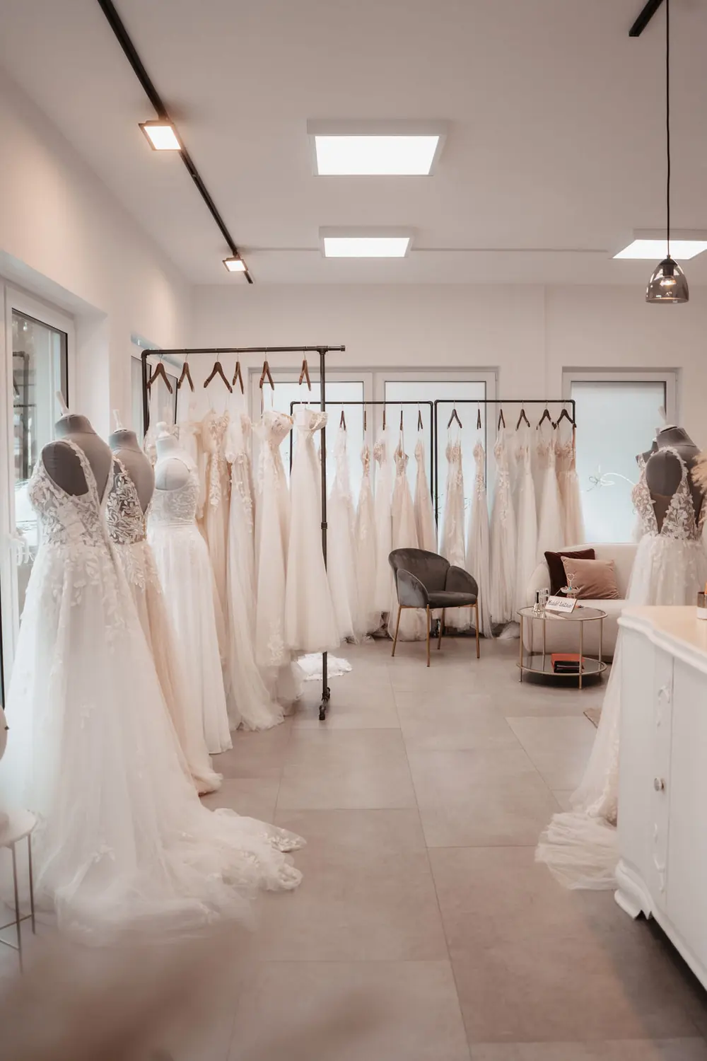 Der Verkaufsraum von Glücksmoment Brautmode in Oldenburg: Brautkleider an langen Stangen, Büsten mit Spitzenkleidern und im Hintergrund die Sitzecke.